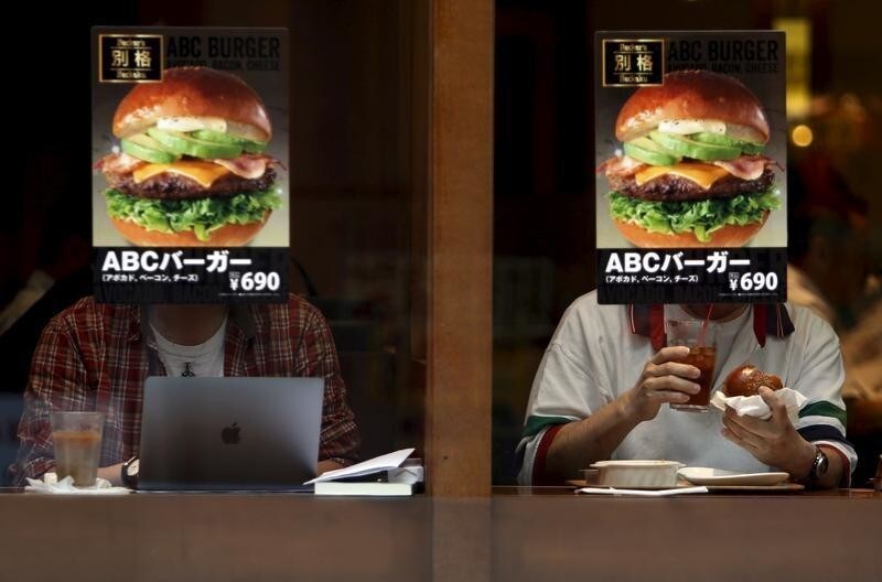 Customers sitting inside a fast food shop are seen behind its hamburger advertisement poster on a window at the Tokyo's Akihabara shopping district, Japan, May 19, 2015. Japan's economy grew at a 2.4 percent annualized rate in the January-March period, expanding for a second straight quarter on a pick-up in capital spending, the government said on Wednesday. Picture taken May 19, 2015. REUTERS/Yuya Shino - GF10000100369