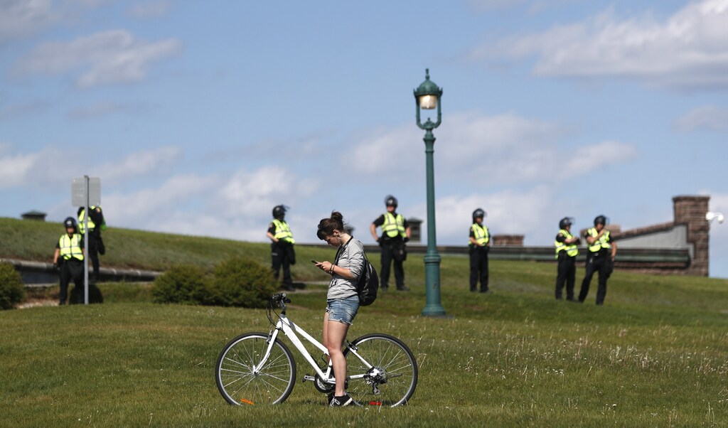A cyclist checks her phone as police stand guard on the Plains of Abraham during a march at the G7 Summit in Quebec City, Quebec, Canada, June 8, 2018. REUTERS/Mathieu Belanger - HP1EE681K0J50