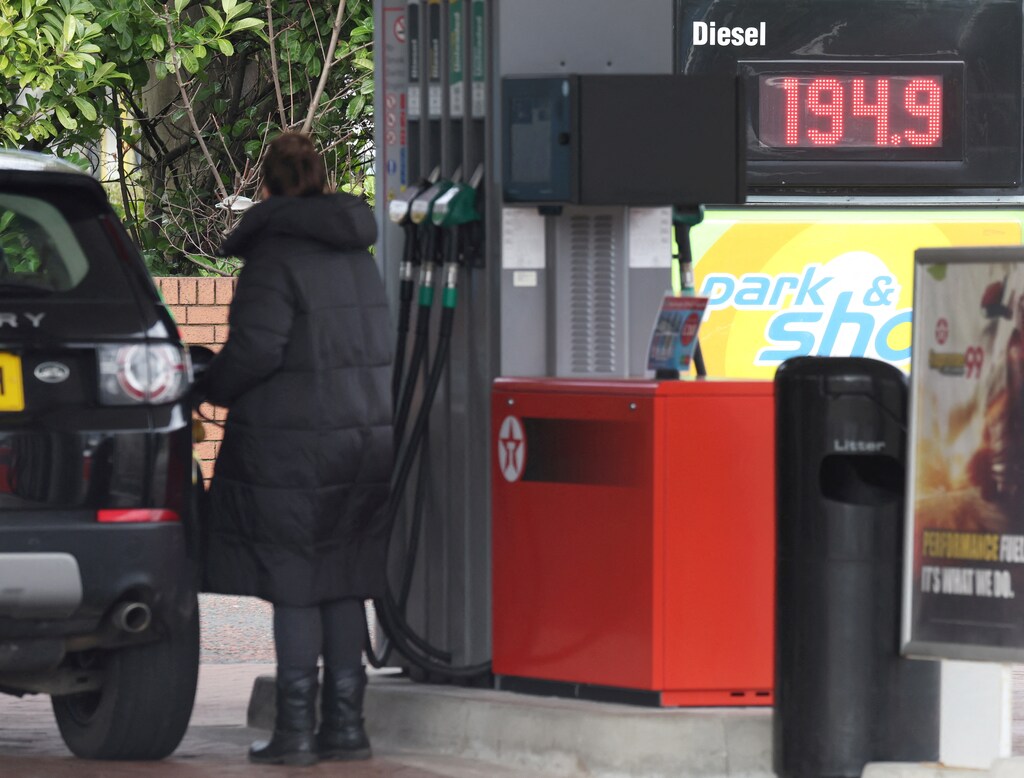 A woman fills up her car in front of a sign showing increased fuel prices at a petrol station in the UK.