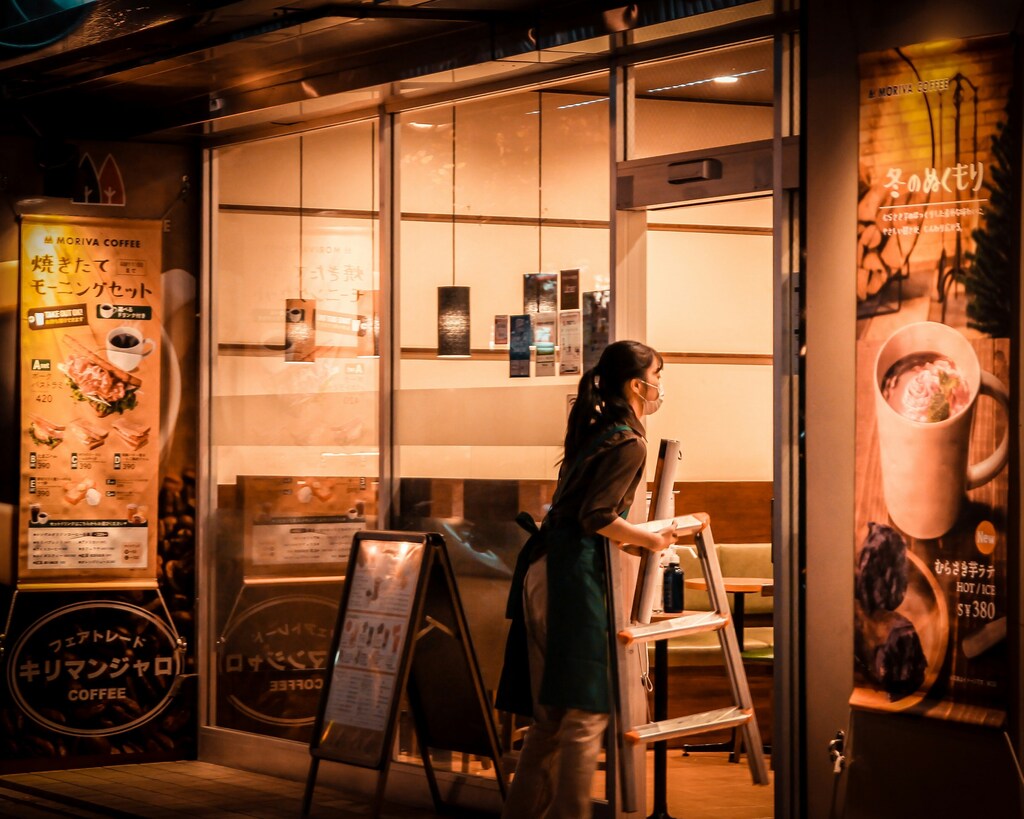 A woman taking a step ladder into a coffee shop at night in Japan: Short-term job matching services are increasingly serving rural communities in Japan.