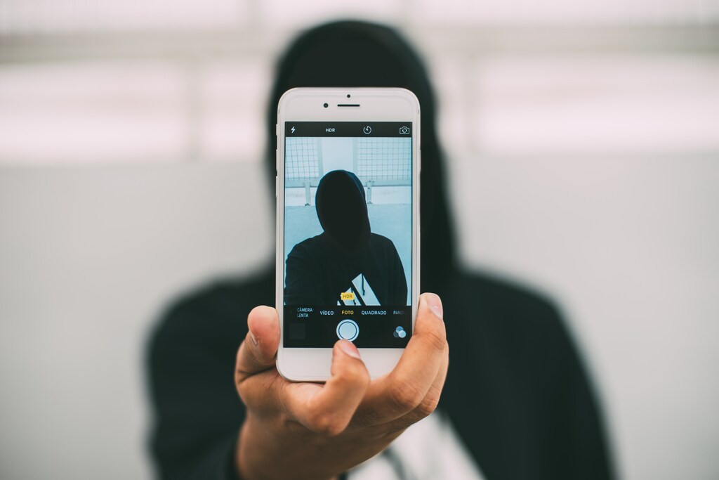 A person in a hoodie takes a selfie with a smartphone