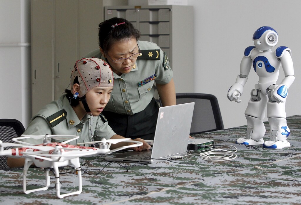 A student (L) and an instructor look at a computer as they demonstrate using a headset to control robots with her mind, at the People's Liberation Army (PLA) Information Engineering University, in Zhengzhou, Henan province, China, August 7, 2015. The robots can be controlled through the headset to go different directions, turn their heads and pick up objects, local media reported. Picture taken August 7, 2015. REUTERS/Stringer CHINA OUT. NO COMMERCIAL OR EDITORIAL SALES IN CHINA TPX IMAGES OF THE DAY - RTX1NV1C