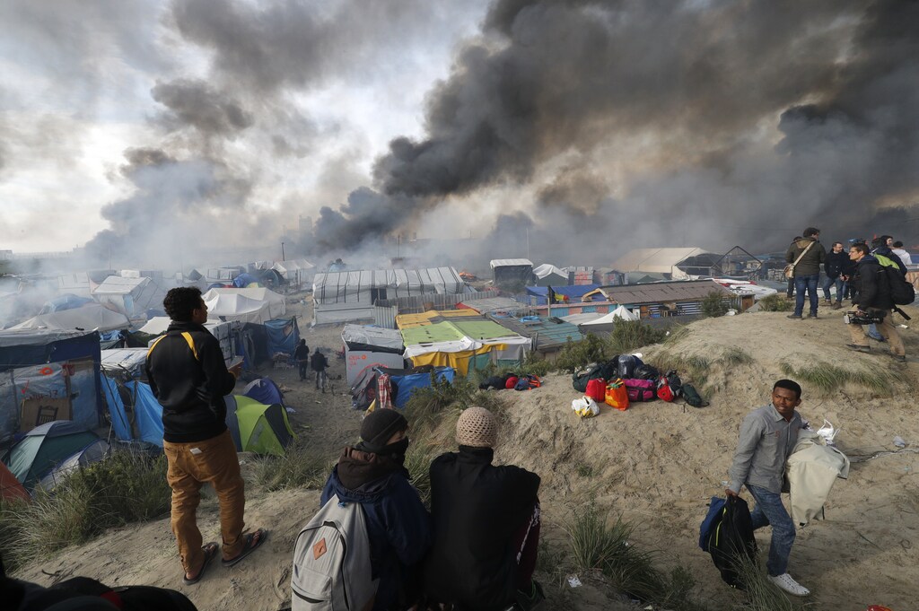 Smoke rises the sky as migrants and journalists look at burning makeshift shelters and tents in the "Jungle" on the third day of their evacuation and transfer to reception centers in France, as part of the dismantlement of the camp in Calais, France, October 26, 2016. REUTERS/Philippe Wojazer TPX IMAGES OF THE DAY - LR1ECAQ0UA87V