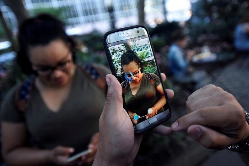 A Pokemon appears on the screen next to a woman as a man plays the augmented reality mobile game "Pokemon Go" by Nintendo in Bryant Park in New York City, U.S. July 11, 2016.