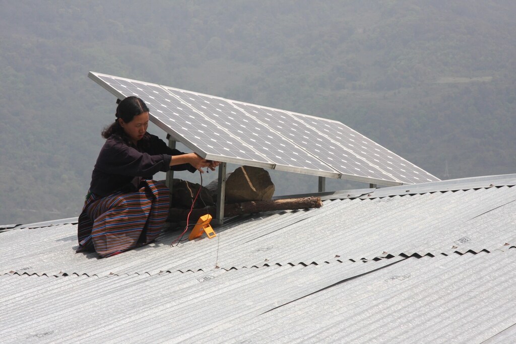 Una mujer instala un panel fotovoltaico en el techo de su casa.