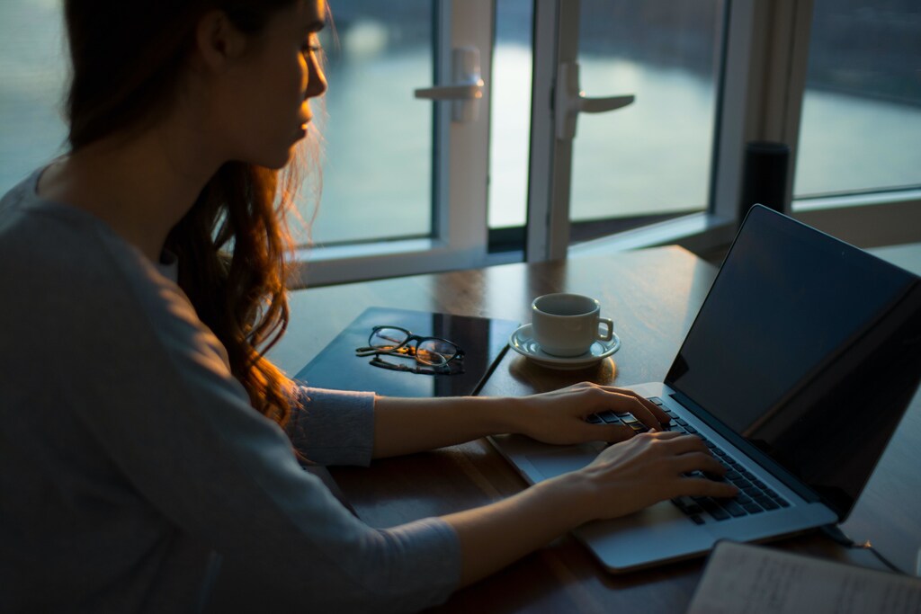 Person sat at a desk with a laptop and hot drink