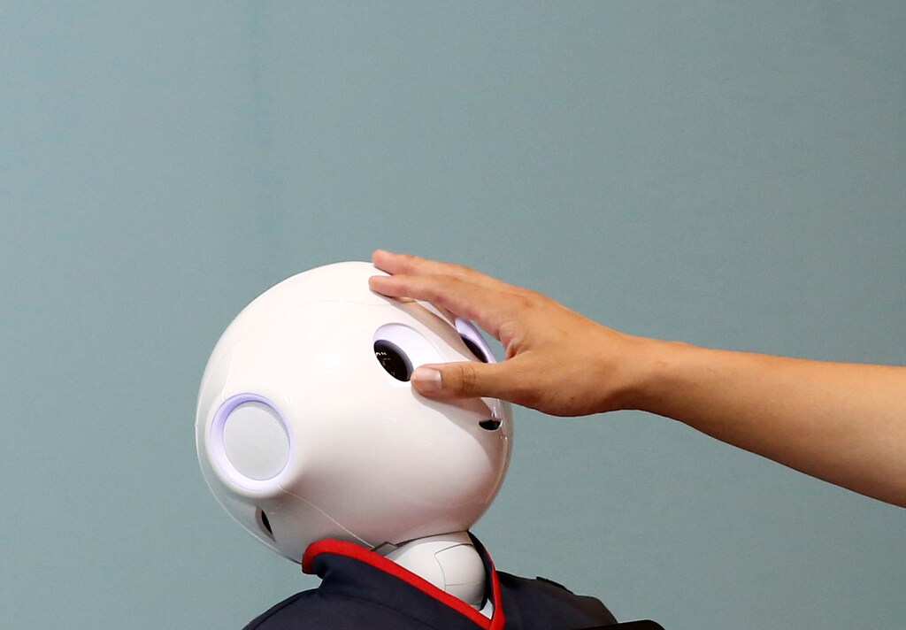 A man touches the head of a SoftBank humanoid robot known as Pepper at the venue for Pepper World 2016 Summer.