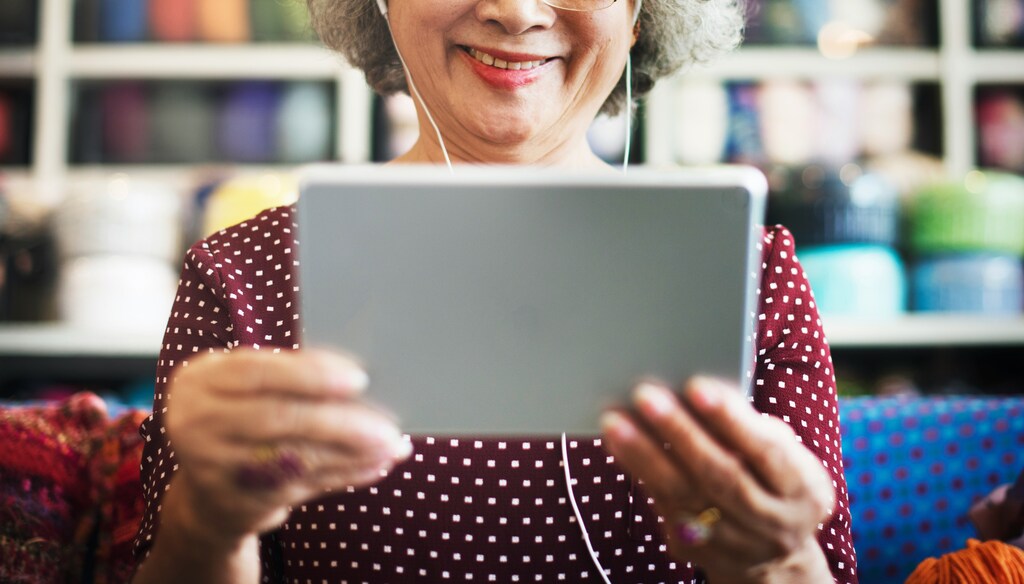 Older woman looking at tablet on sofa: Digital speech biomarkers offer a promising tool for the screening and monitoring of neurodegenerative disorders