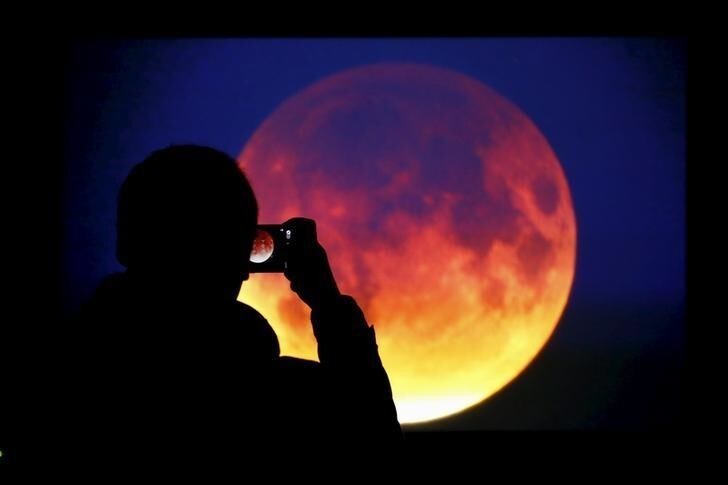 A man takes picture of the screen displaying the moon, appearing in a dim red colour, which is covered by the Earth's shadow during a total lunar eclipse in Warsaw, Poland September 28, 2015. Sky-watchers around the world were treated when the shadow of Earth cast a reddish glow on the moon, the result of rare combination of an eclipse with the closest full moon of the year. The total "supermoon" lunar eclipse, also known as a "blood moon" is one that appears bigger and brighter than usual as it reaches the point in its orbit that is closest to Earth. REUTERS/Kacper Pempel