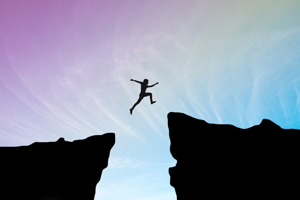 Man jump through the gap between hill.man jumping over cliff on sunset background.