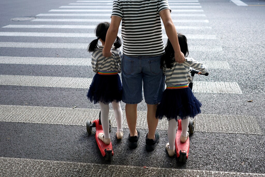 A father crosses a road with his twin daughters in Shanghai, China September 28, 2018.