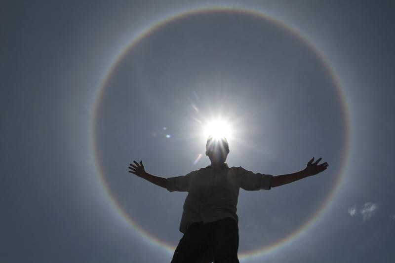 A man poses for photos as solar halo is seen in the sky of Brasilia September 30, 2011. This weather phenomenon creates rainbows around the sun, and according to meteorologist, halo is formed by the reflection of ice crystals. REUTERS/Ueslei Marcelino (BRAZIL - Tags: ENVIRONMENT TPX IMAGES OF THE DAY) - RTR2S1UT