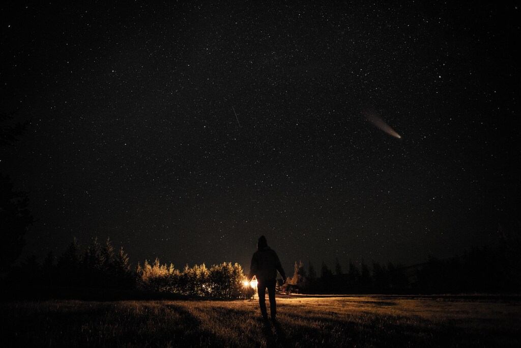 A person stands at night, looking at an asteroid.