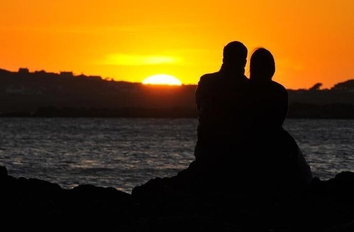 A couple watch the sun setting on a beach near Holyhead in Anglesey, north Wales May 1, 2011. Britain's Prince William, the Duke of Cambridge, is stationed as a helicopter pilot on Anglesey and will return to work this week following his marriage to Kate Middleton, the Duchess of Cambridge, on April 29. REUTERS/Toby Melville (BRITAIN - Tags: ENVIRONMENT SOCIETY ROYALS)