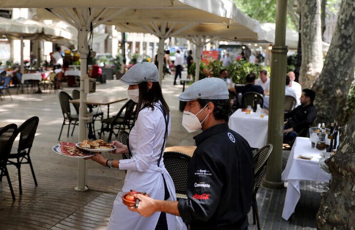 Waiters wearing protective face masks carry food for clients at an outdoor seating section of a restaurant at Ramblas, as some Spanish provinces are allowed to ease lockdown restrictions during phase one, amid the coronavirus disease (COVID-19) outbreak, in Barcelona, Spain, May 25, 2020.