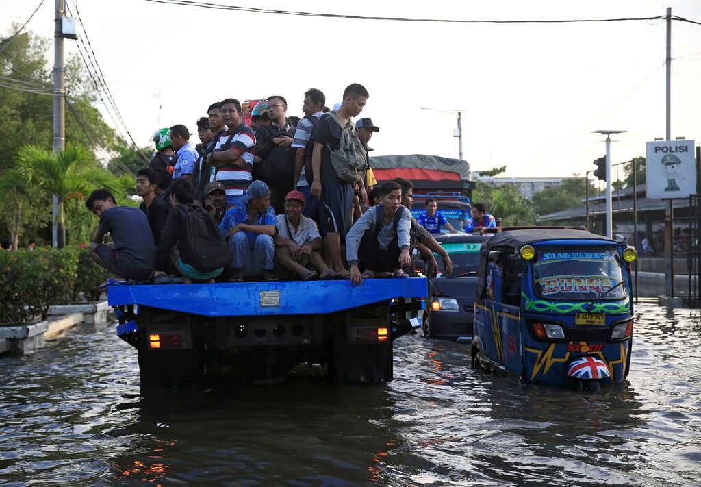 Workers being transported at the back of a truck on a flooded street after high tide hit Muara Baru area in Jakarta, Indonesia, December 6, 2017. REUTERS/Beawiharta - RC1E55986540