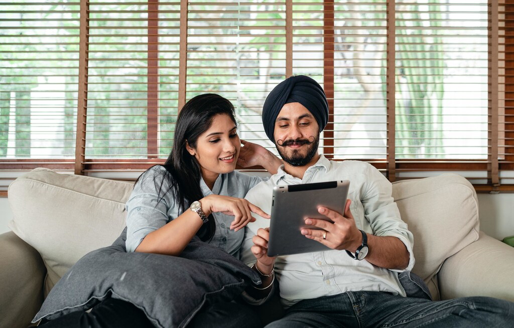 Indian man and women sitting on sofa while looking at electronic tablet.