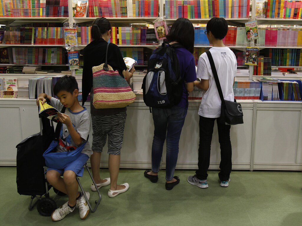 A boy reads beside parents choosing children's books inside the Hong Kong Book Fair July 18, 2012. More than 530 exhibitors from 23 countries and regions took part in the territory's biggest book fair, which opened on Tuesday through July 24. REUTERS/Bobby Yip (CHINA - Tags: MEDIA) - RTR351AU