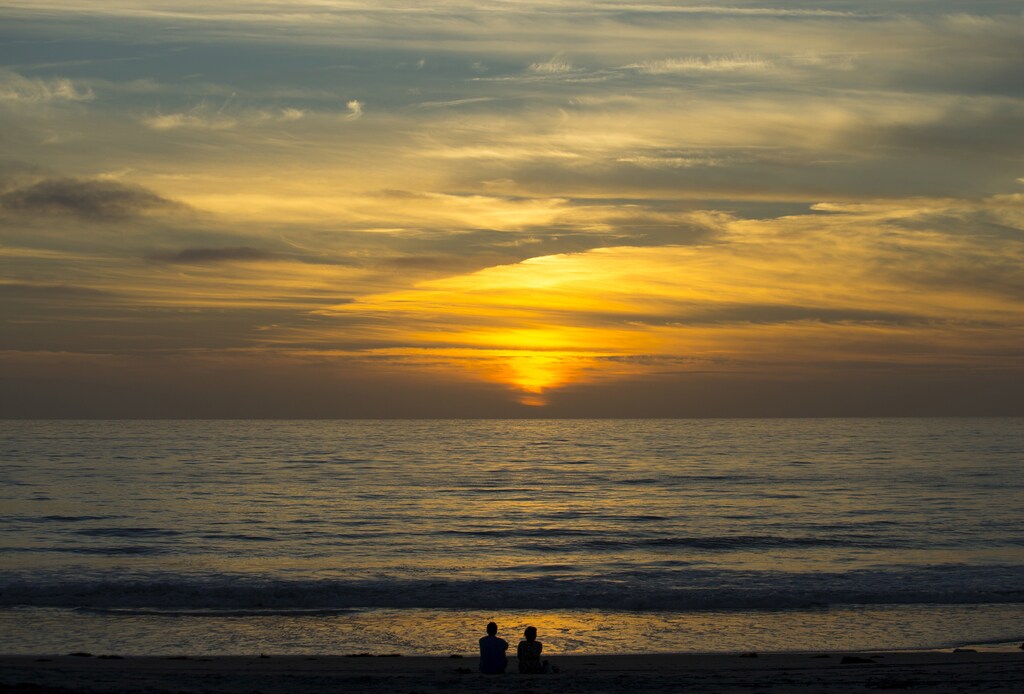 A couple sit on the sand watching the sun set on the Pacific Ocean in Cardiff, California September 27, 2015. REUTERS/Mike Blake - GF10000224609