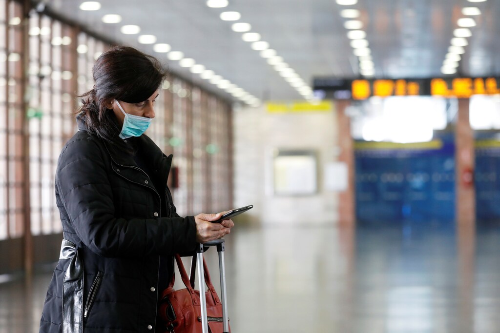 A woman in a protective mask checks her phone at the Messina Station in the Sicilian city of Messina after Sicily requested that transport to the island would be blocked from mainland Italy as part of measures to contain coronavirus contagion on the island, in Messina, Italy March 16, 2020. REUTERS/Antonio Parrinello - RC2ZKF9GSWSH