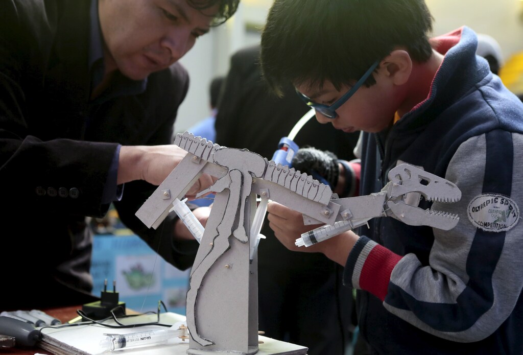 A student is helped by his teacher to build a dinosaur robot during the annual robotics fair in Bolivia