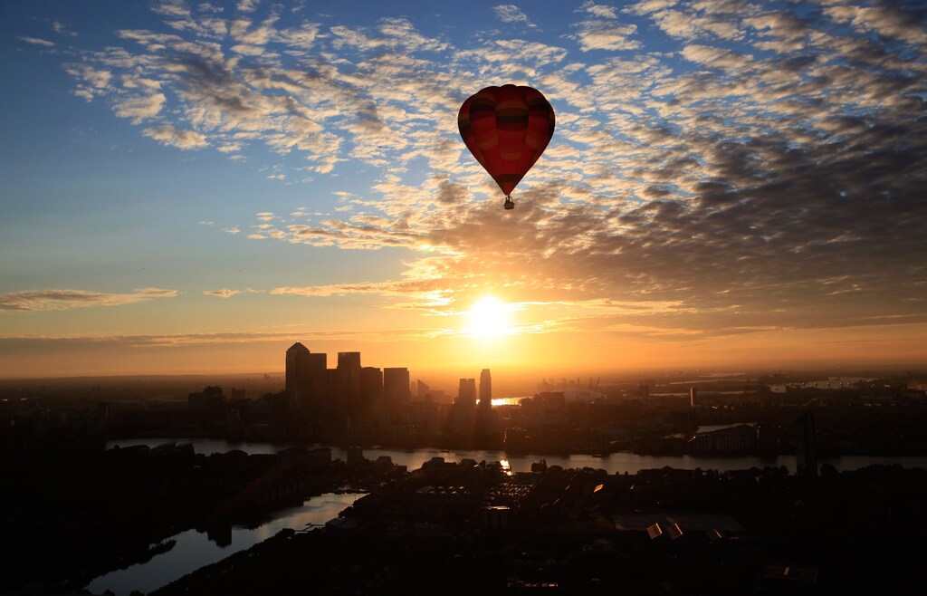 A hot air balloon rises into the early morning sky in front of the Canary Wharf financial district of London, July 25, 2011.
