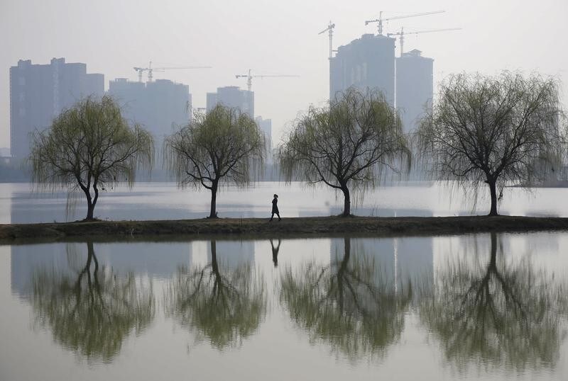 A woman walks past trees reflected on a lake in front of a construction site of a residential compound on a hazy day in Wuhan, Hubei province March 6, 2015. China aims to grow its economy by around 7 percent in 2015 and to keep consumer inflation at around 3 percent, Premier Li Keqiang said in remarks prepared for delivery at today's opening of the annual meeting of parliament, the National People's Congress. REUTERS/Stringer (CHINA - Tags: ENVIRONMENT BUSINESS CONSTRUCTION REAL ESTATE TPX IMAGES OF THE DAY) CHINA OUT. NO COMMERCIAL OR EDITORIAL SALES IN CHINA - GM1EB36182X01