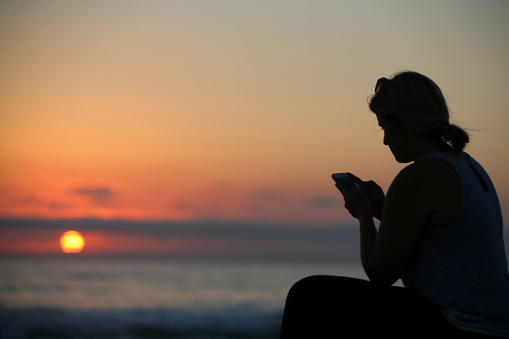A women looks at her mobile phone as the sun sets over the ocean in Encinitas, California, U.S., July 5, 2017.