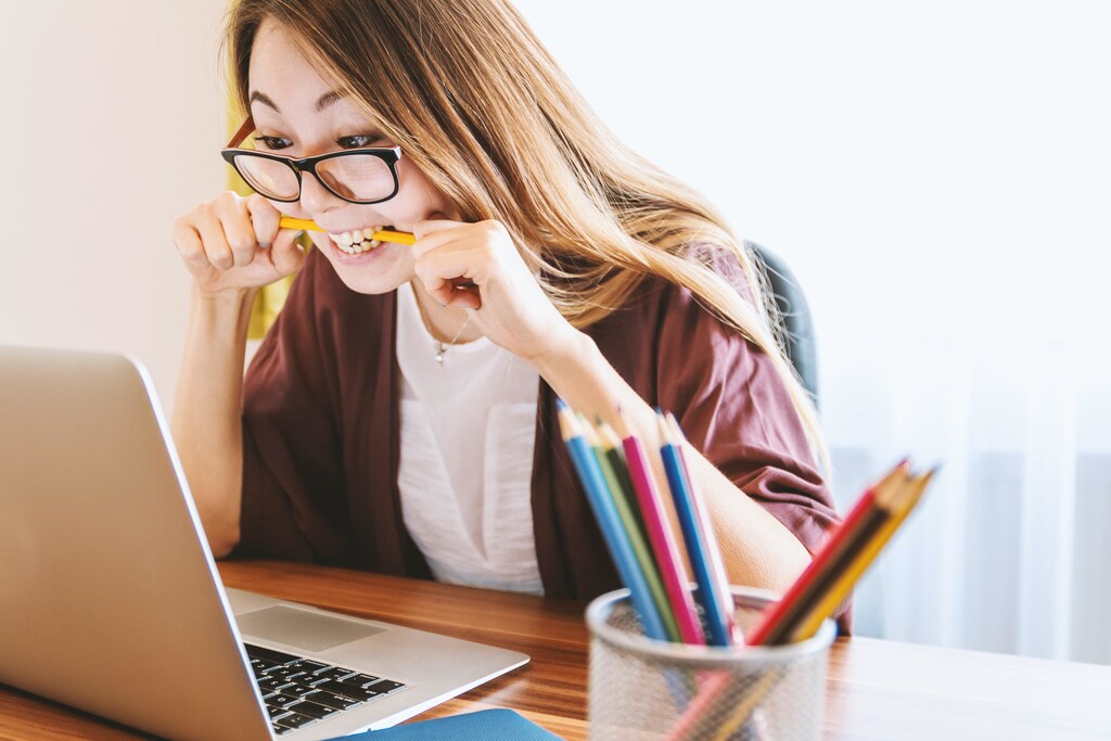 A woman biting a pencil in frustration while staring at laptop screen.
