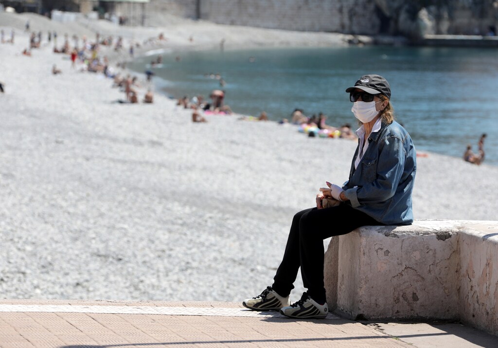 A woman, wearing a protective face mask, sits on the beach of the Promenade des Anglais, after France reopened its beaches to the public as it softens its strict lockdown rules following the outbreak of the coronavirus disease (COVID-19), in Nice, France, May 21, 2020. REUTERS/Eric Gaillard - RC2ZSG9X2R5J