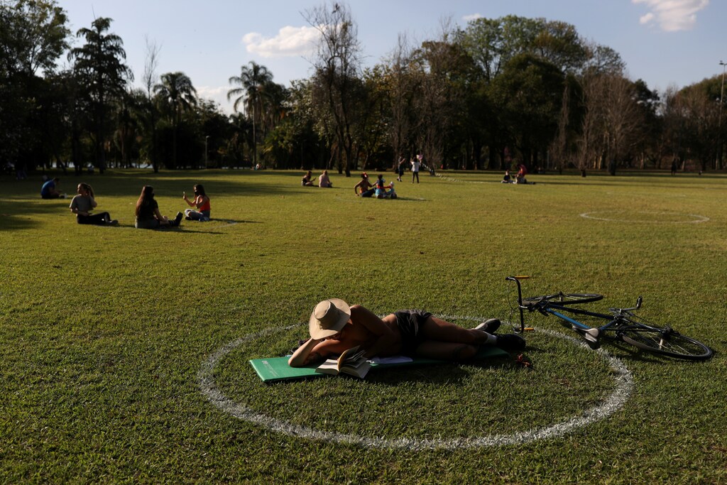 A man reads as he lies in a field where circles were painted to help visitors maintain social distancing at Ibirapuera Park after it was reopened as the city eases the restrictions imposed to control the spread of the coronavirus disease (COVID-19), in Sao Paulo, Brazil July 13, 2020. REUTERS/Amanda Perobelli TPX IMAGES OF THE DAY - RC2JSH94FV6X
