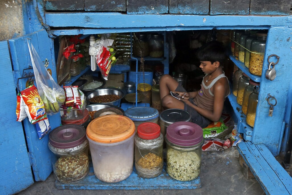 A boy uses a mobile phone as he sits inside his father's snacks shop along a road in Kolkata, India, February 22, 2016. REUTERS/Rupak De Chowdhuri TPX IMAGES OF THE DAY - RTX27ZEW