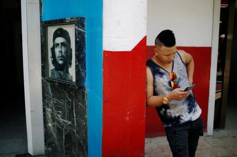 A young Cuban checks his phone at an internet hotspot next to a picture of late revolutionary hero Ernesto "Che" Guevara in Havana, Cuba August 10, 2018. Picture taken August 10, 2018. REUTERS/Tomas Bravo - RC1101C97990