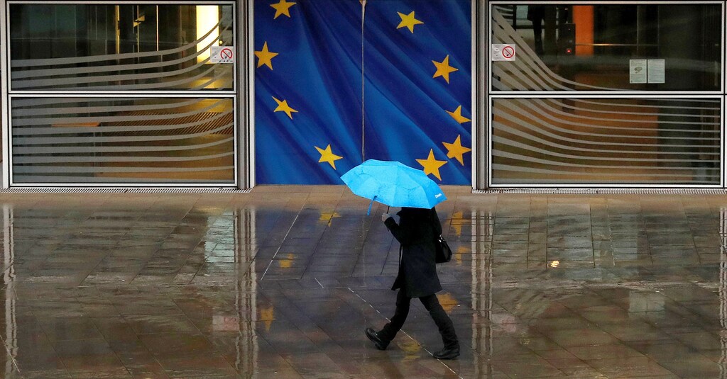 A woman holds an umbrella as she walks past the flag of the European Union outside the European Commission in Brussels, Belgium, December 13, 2017. REUTERS/Phil Noble - RC1C3CCB98C0