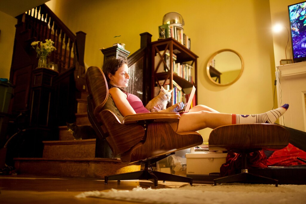 A woman works from home, reclined in a chair with her cat in her lap.