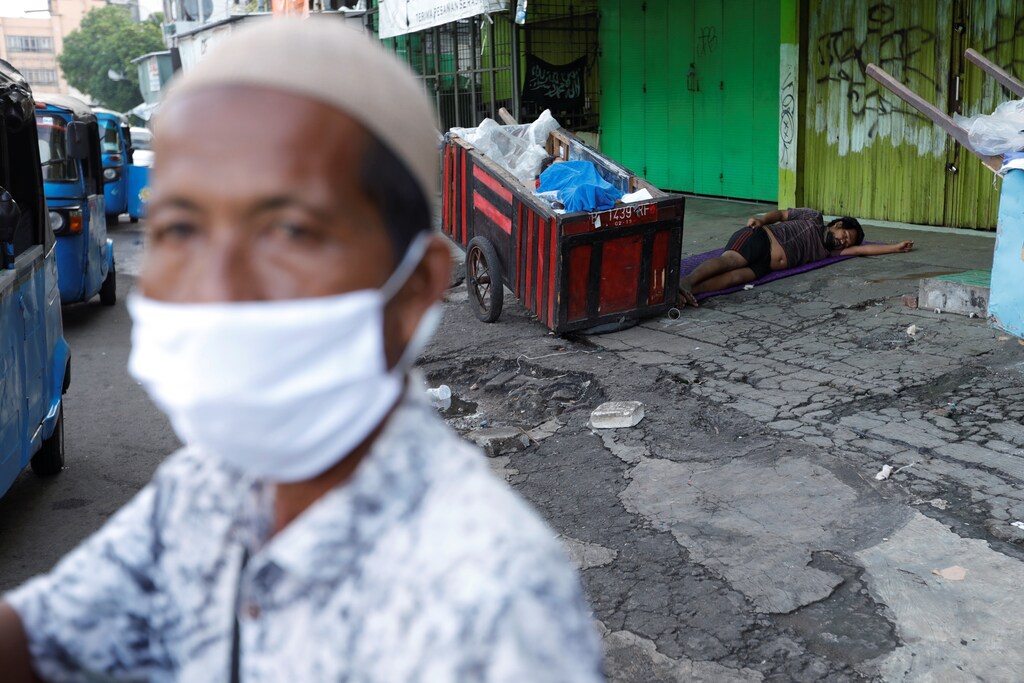 Homeless people sleep on a street while a street vendor wearing a face mask looks on outside a closed store, amid coronavirus disease (COVID-19) outbreak, at Tanah Abang textile market in Jakarta, Indonesia, March 31, 2020. REUTERS/Willy Kurniawan - RC2VUF91YDZ9