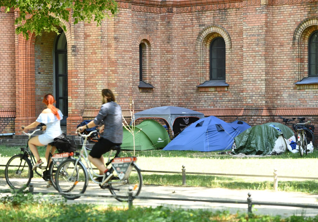 Cyclists pass by tents of homeless people in front of St. Thomas Church in Berlin, Germany women business businesswoman businessman corporation corporate finance wall street stock exchange capitalism private ownership board c-suite ceos cfos corporation united states us america wall street change gender parity equality goldman sachs davos industry representation fair finance fiscal financial economics economies trading trade price money profit value men male female change changing 2020 future