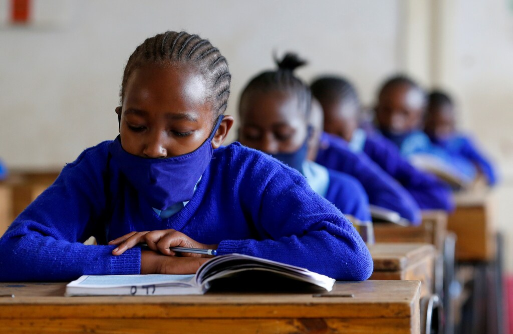 A schoolgirl wears a face mask as she reads a book inside a classroom at the Olympic Primary School during the partial reopening of schools, after the government scrapped plans to cancel the academic year due to the coronavirus disease (COVID-19) pandemic, in Kibera slums of Nairobi, Kenya October 12, 2020. REUTERS/Thomas Mukoya - RC2WGJ9PLMPT