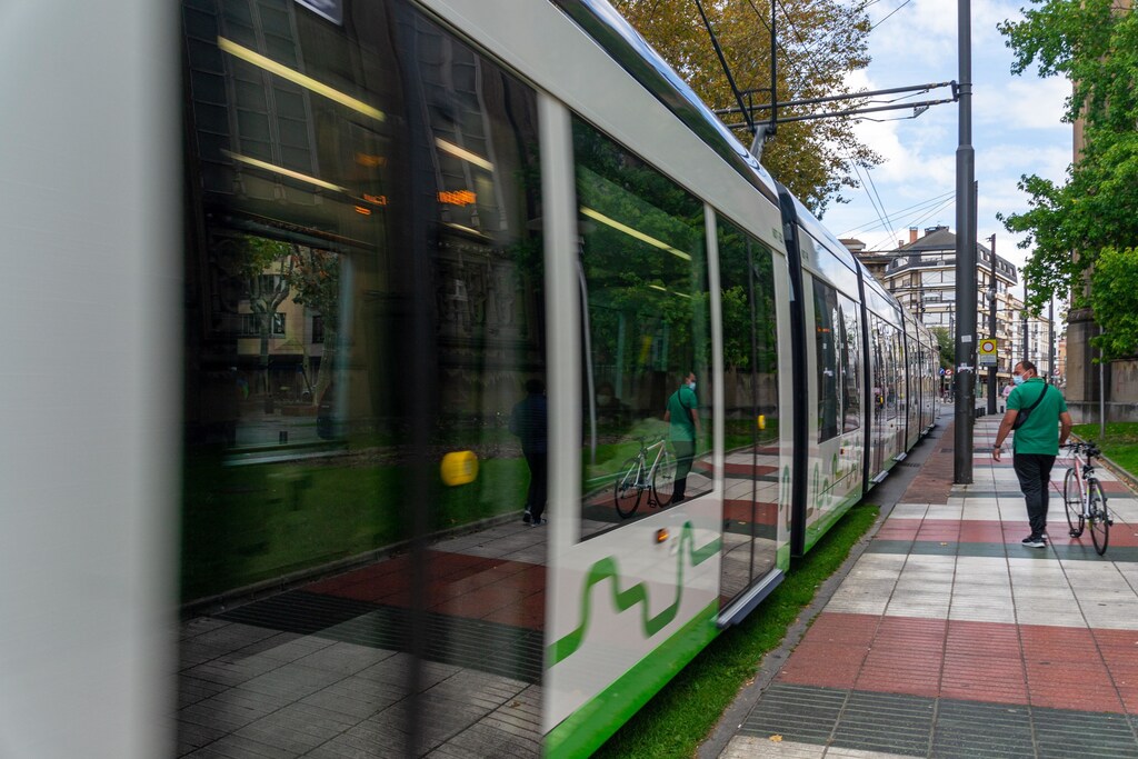 A green and white tram with man walking a bike next to it.