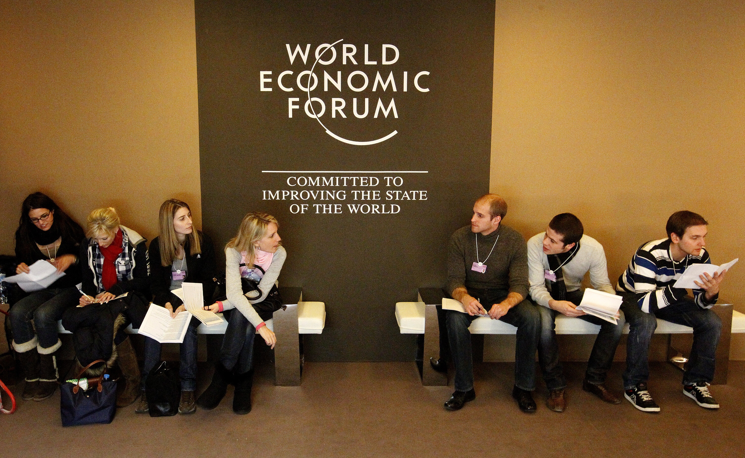 A group of people sits in front of the logo of the World Economic Forum (WEF) in the congress centre in the Swiss mountain resort of Davos January 24, 2011. The annual meeting of the WEF takes place under heavy security measures from January 26 to 30 in the Alpine resort, and will be attended by top politicians, monetary policymakers and senior business executives. REUTERS/Arnd Wiegmann (SWITZERLAND - Tags: POLITICS BUSINESS)