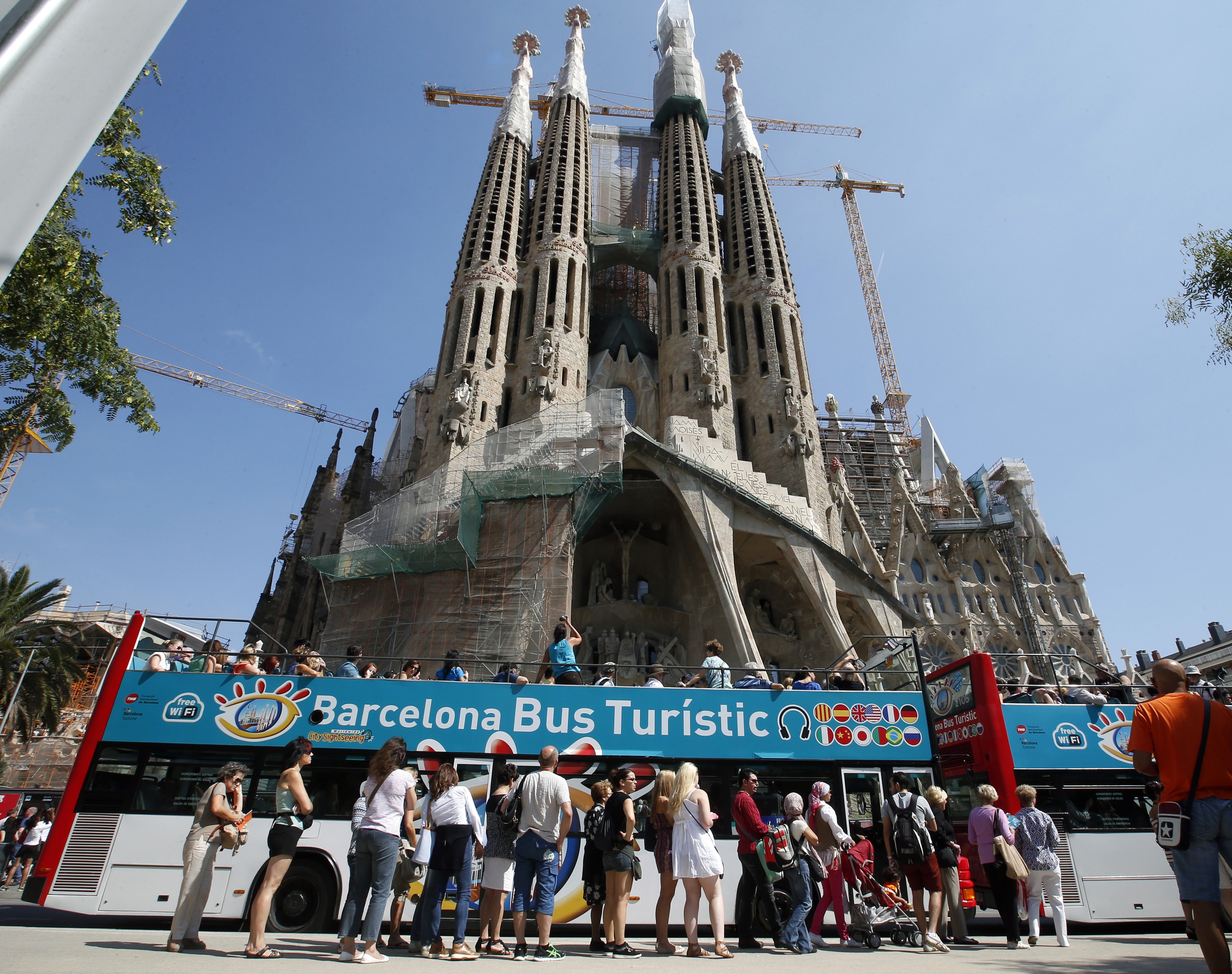 People queue up at a city tour bus stop in front of the Basilica Sagrada Familia in Barcelona, September 13, 2013. Sunseekers spurning unrest in Egypt and Turkey flocked to Spain in record numbers in August, setting the country up for its best-ever year for visitors and giving a boost to the ailing economy. Tourism contributed over 5 percent of Spain's economy or GDP in 2012 and provided around 900,000 jobs, according to Euromonitor, in a country where one in four is out of work, meaning a boost to tourist figures should be good news as other sectors flag. Picture taken September 13, 2013.  REUTERS/Albert Gea (SPAIN - Tags: TRAVEL BUSINESS) - RTX13WQ6         