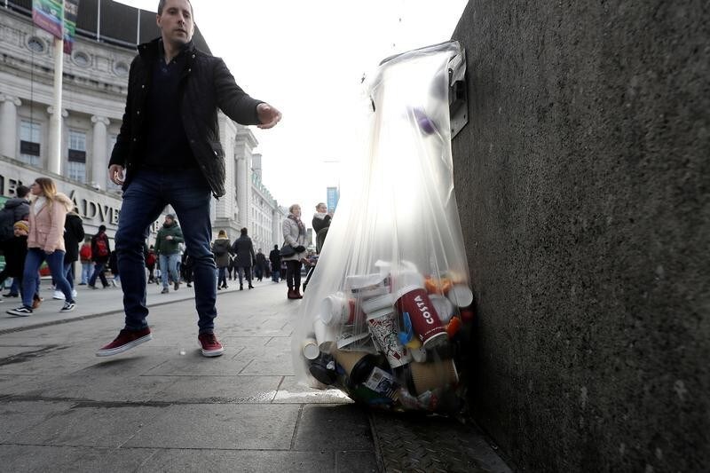 A pedestrian throws a discarded item into a bag containing paper cups alongside other rubbish on the Southbank, in London, Britain January 6, 2018. REUTERS/Simon Dawson - RC1B0A3222C0