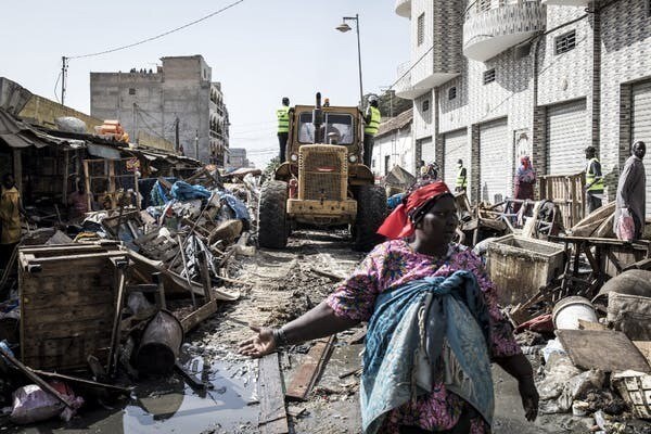 Une femme proteste alors qu’un bulldozer déblaie les étals d’un marché informel avant la désinfection du quartier populaire de la Médina à Dakar, le 22 mars 2020.