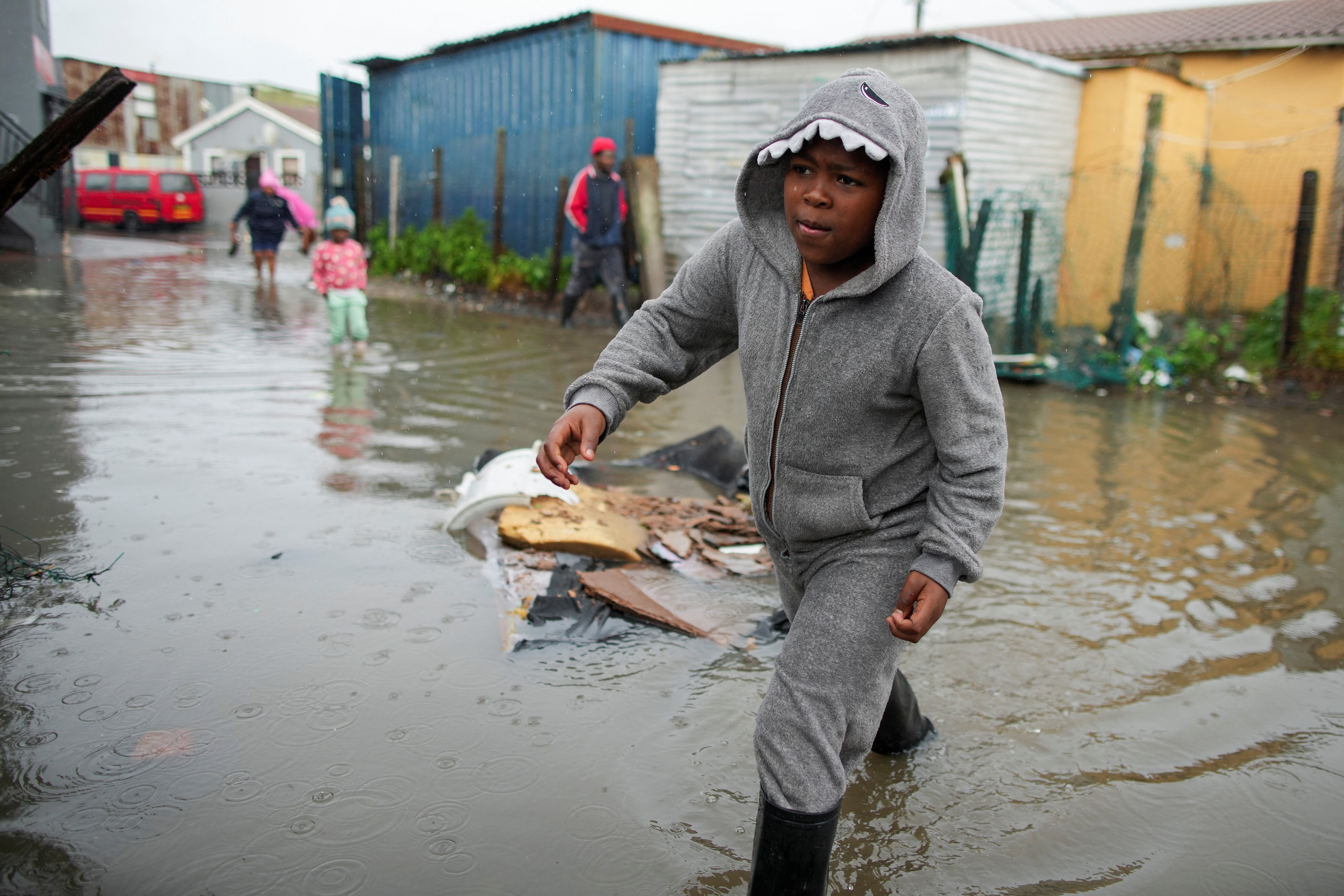 A resident walks across a flooded road following severe weather from a cold front in Masiphumelele, Cape Town, South Africa July 11, 2024