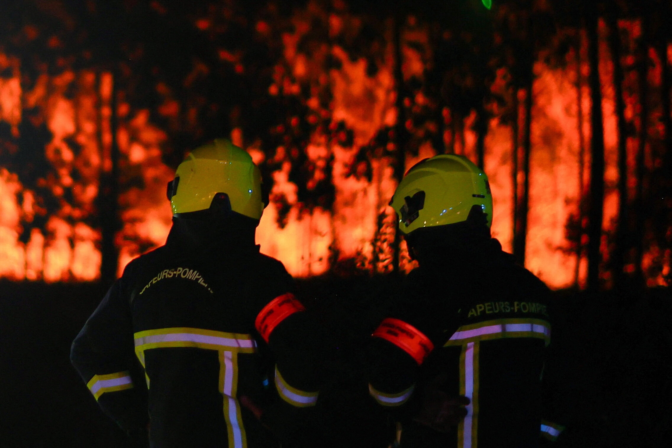 Firefighters stand facing flames at the scene of a wildfire, in Andernos-les-Bains in the Gironde department, amongst worsening drought conditions following a heatwave and water shortages across much of France.