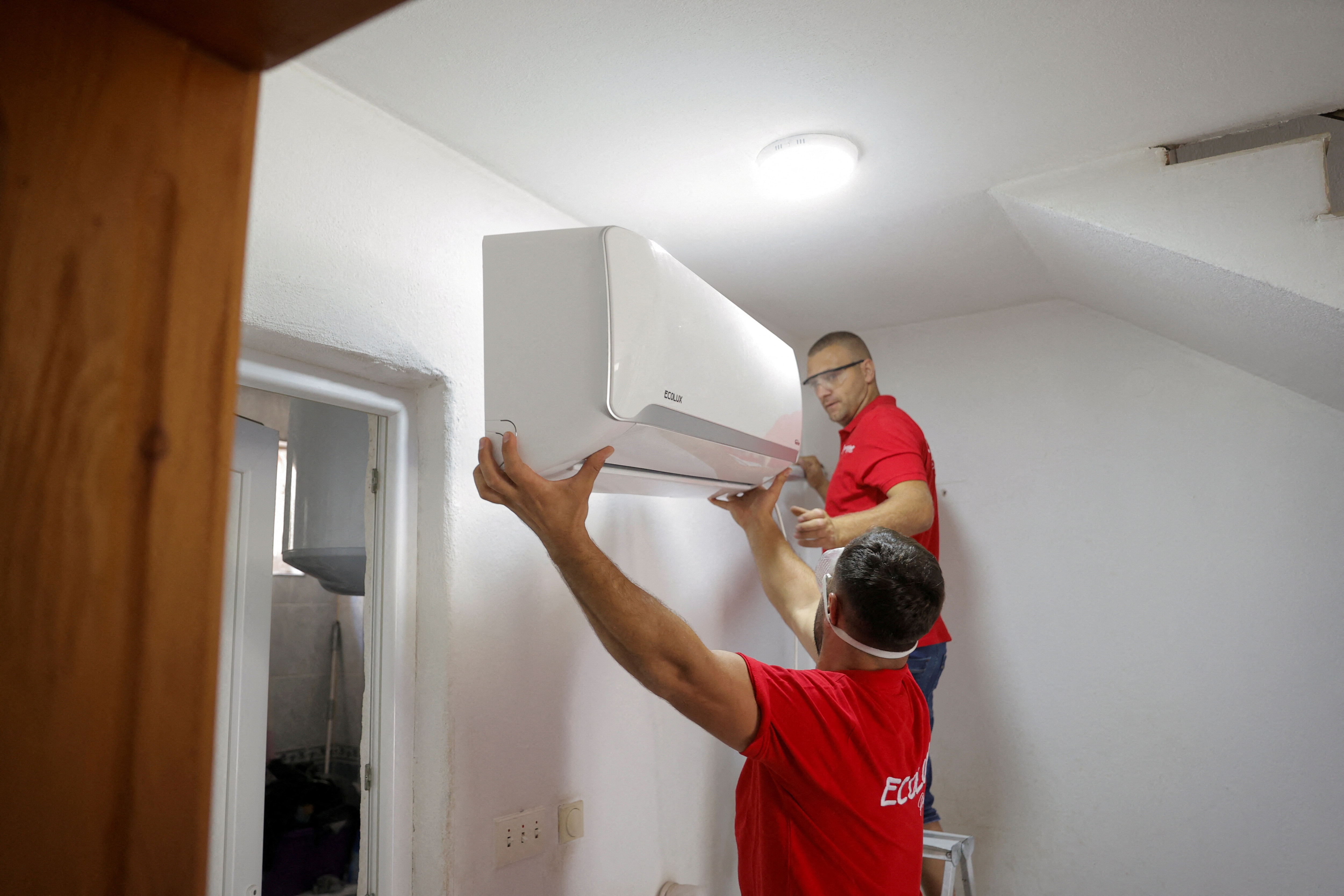 FILE PHOTO: Workers mount an air conditioner unit on a house in the town of Mitrovica, Kosovo July 29, 2024. REUTERS/Valdrin Xhemaj/File Photo