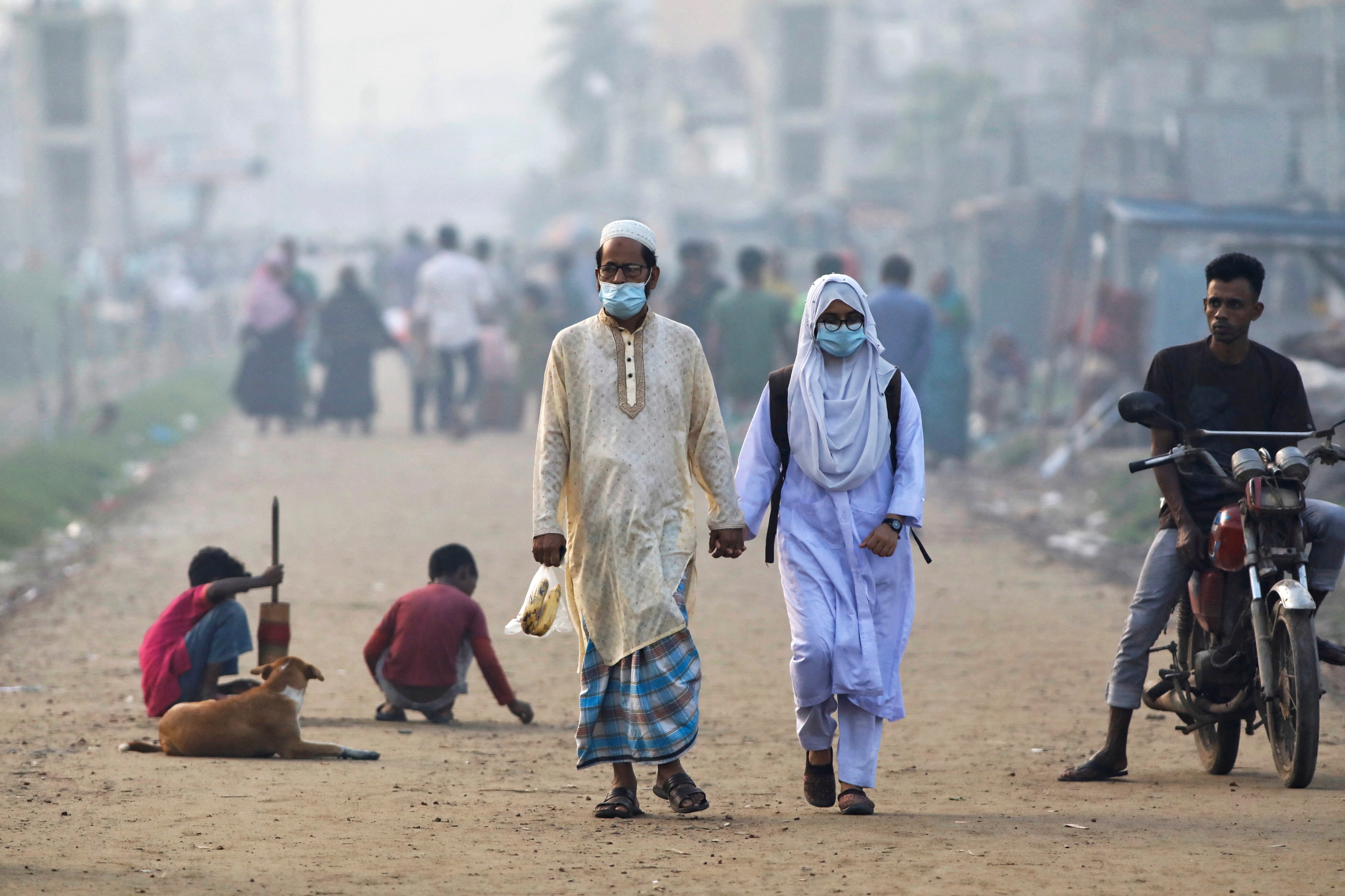 People walk along a road beside a smoky industrial area in Dhaka, Bangladesh, August 3, 2022